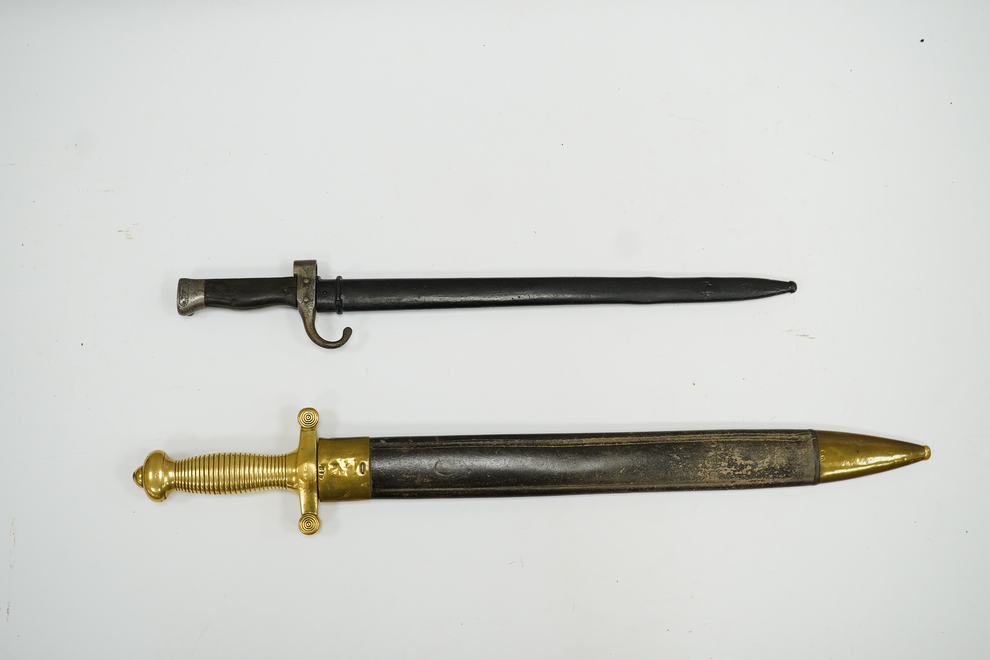 A 19th century French infantryman’s sidearm Gladius with swollen double edged blade, and regulation cast brass cruciform hilt, in its brass mounted leather scabbard, together with a continental bayonet also in scabbard.